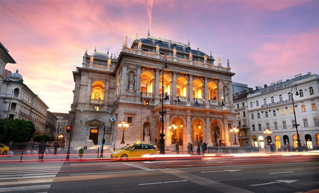 The Hungarian State Opera lit up at dusk, light trails of passing cars in front