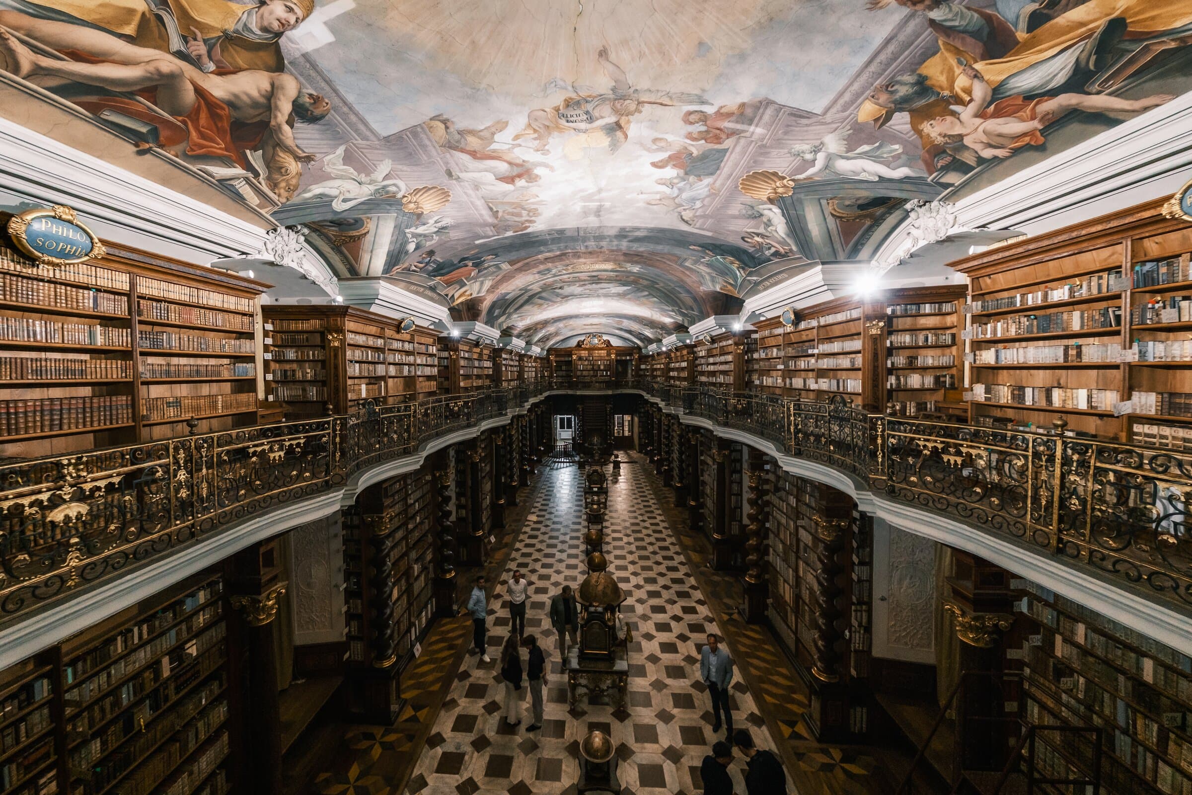 Wide view of a baroque library hall with a gilded gallery and a frescoed vault