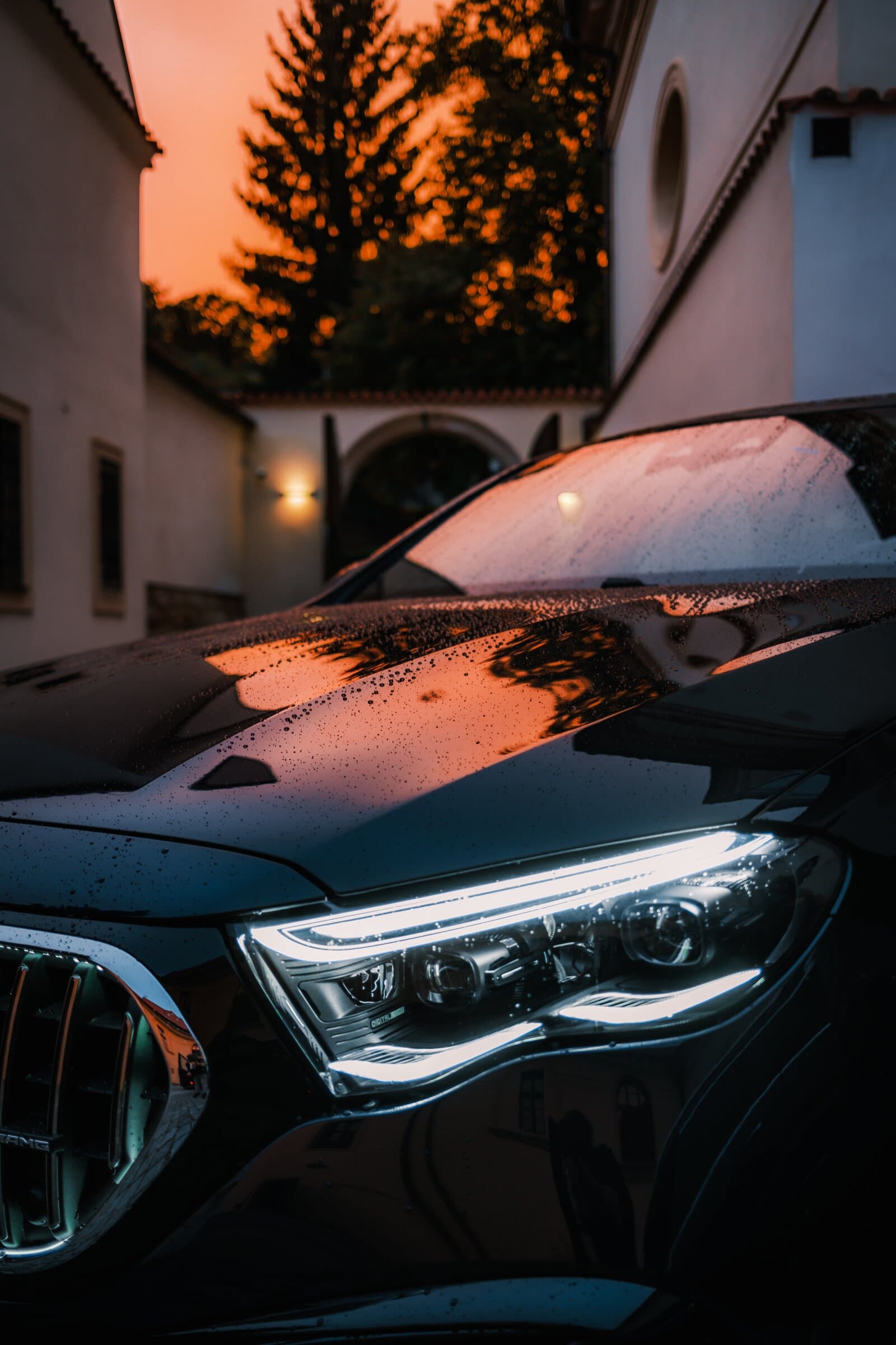 Headlight of a black Mercedes in a courtyard at sunset