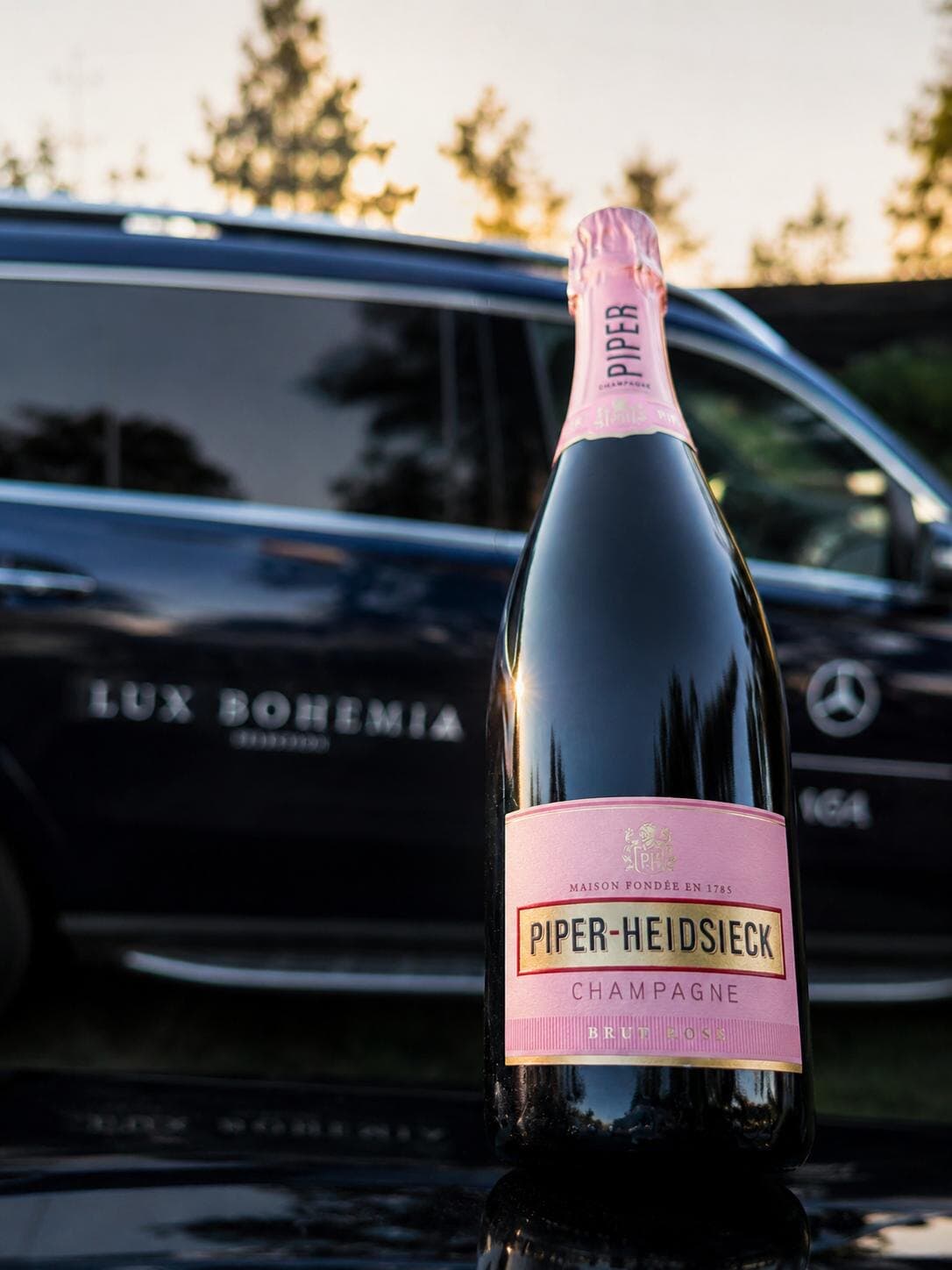 Bottle of Piper-Heidsieck Brut Rosé in front of a black Mercedes with Lux Bohemia lettering