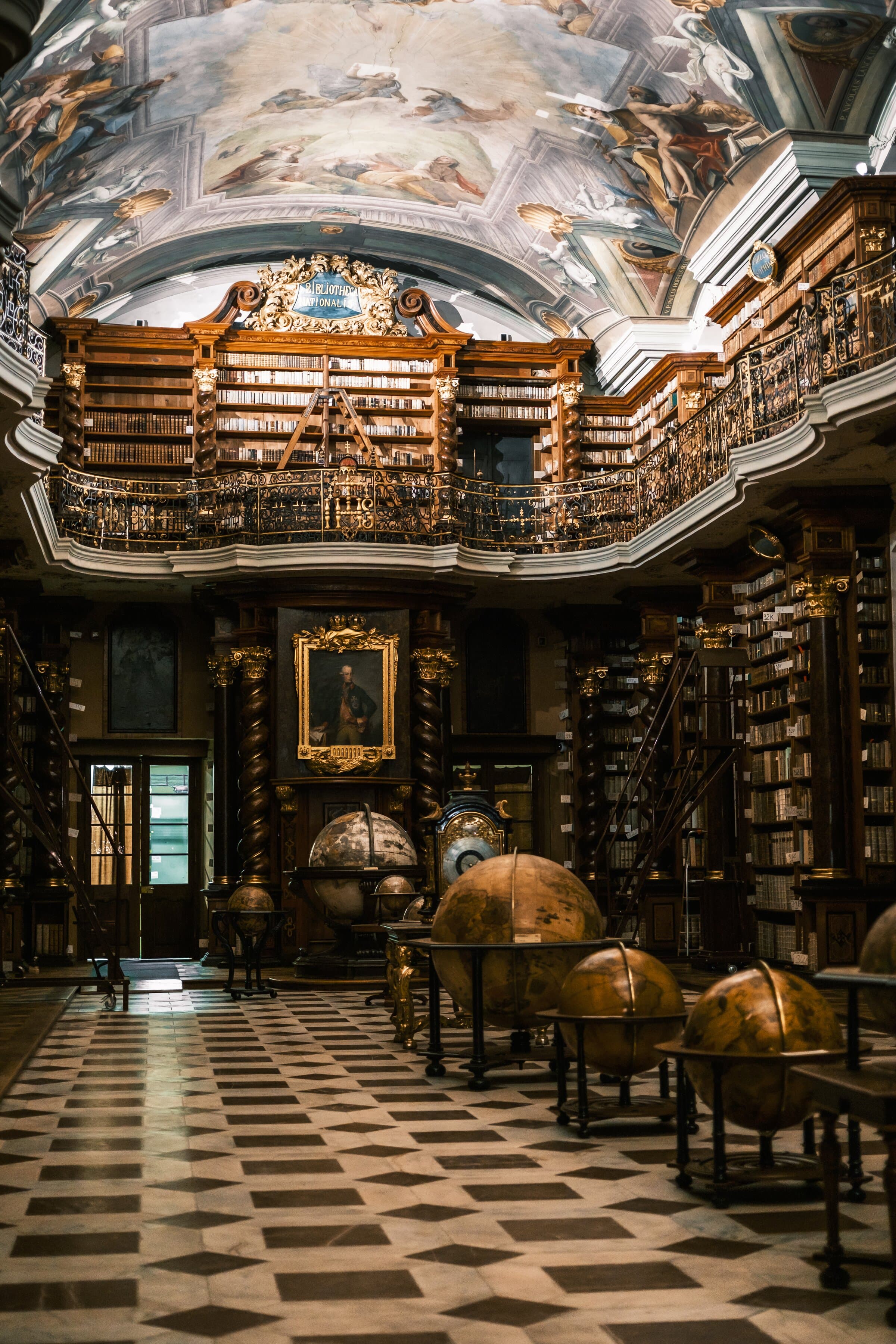 Baroque library hall with a frescoed vault, a gilded gallery and antique globes